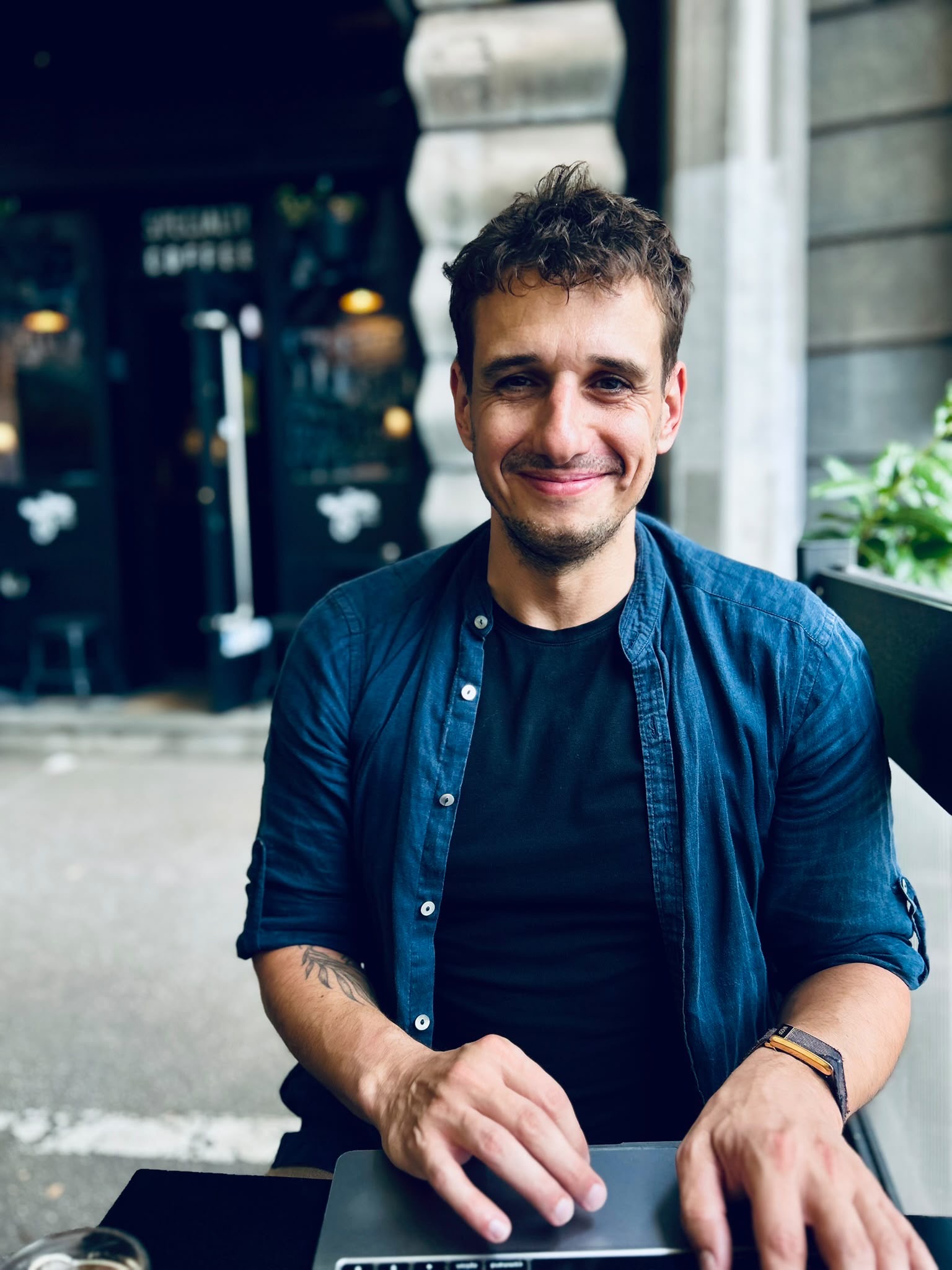 Filip Sardi at a cafe table with a laptop, smiling