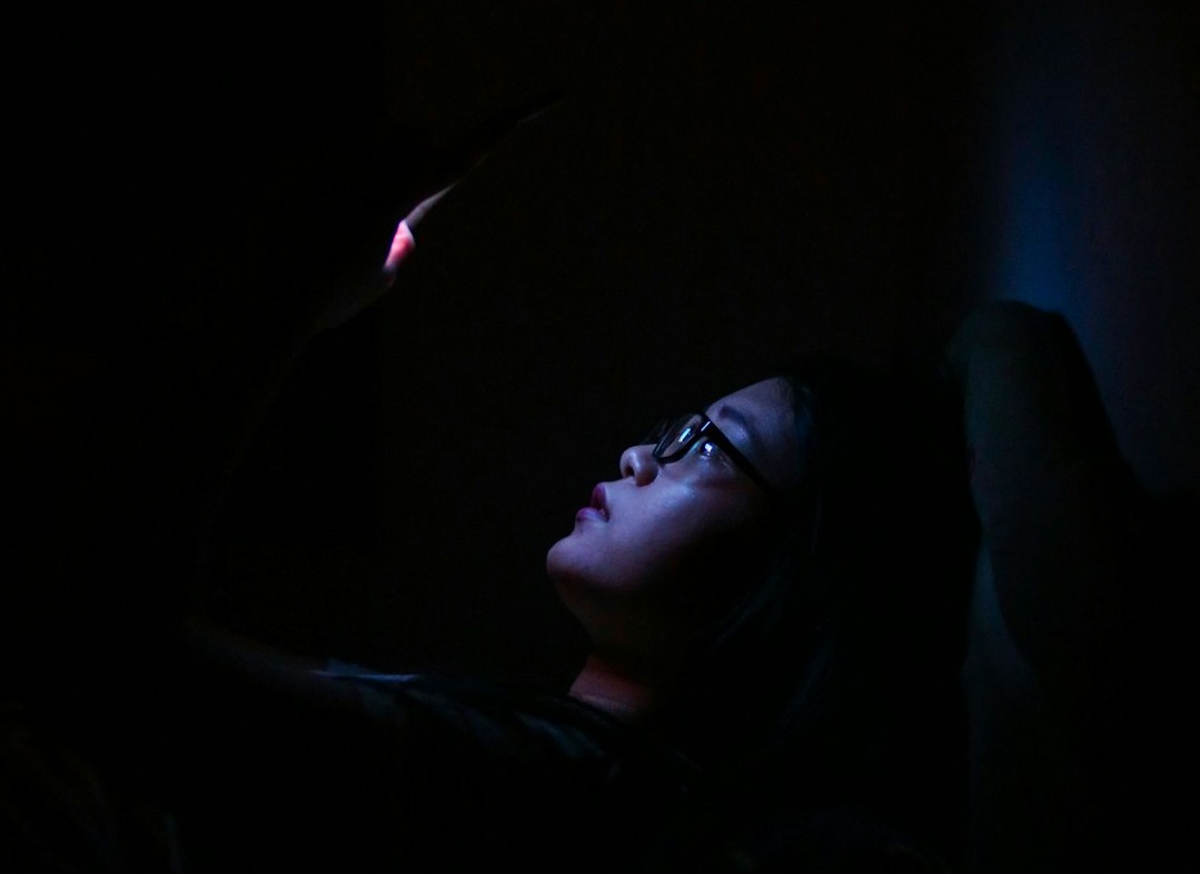A woman in the dark, face lit only by her phone screen