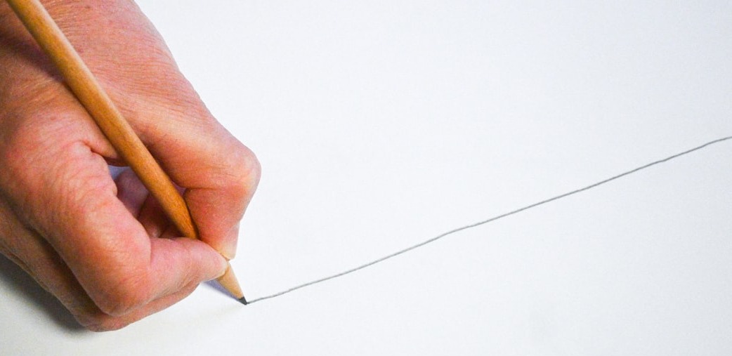 A hand drawing a single pencil line across a blank page